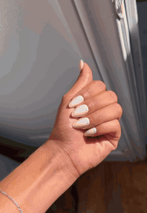 Hand wearing white almond press-on nails with gold-dot details